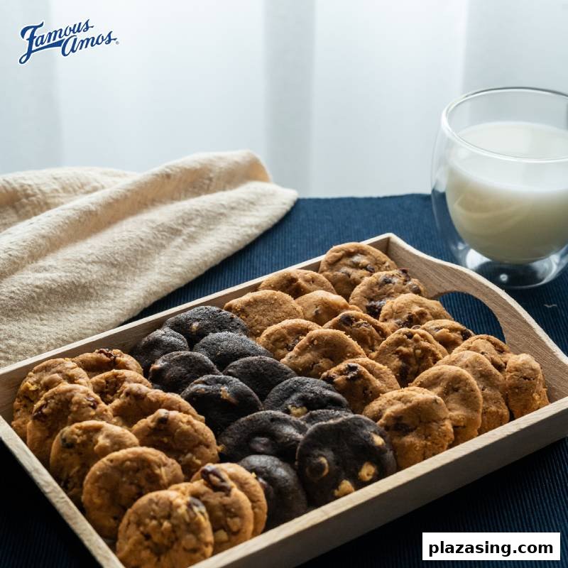 A wooden tray filled with an assortment of freshly baked Famous Amos cookies, accompanied by a glass of milk.