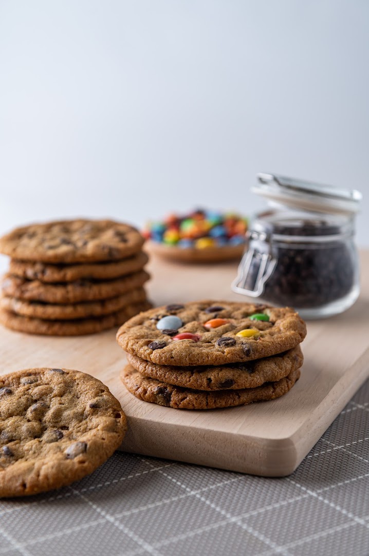 Delicious chocolate chip and M&M cookies stacked on a wooden board, ready to be enjoyed.
