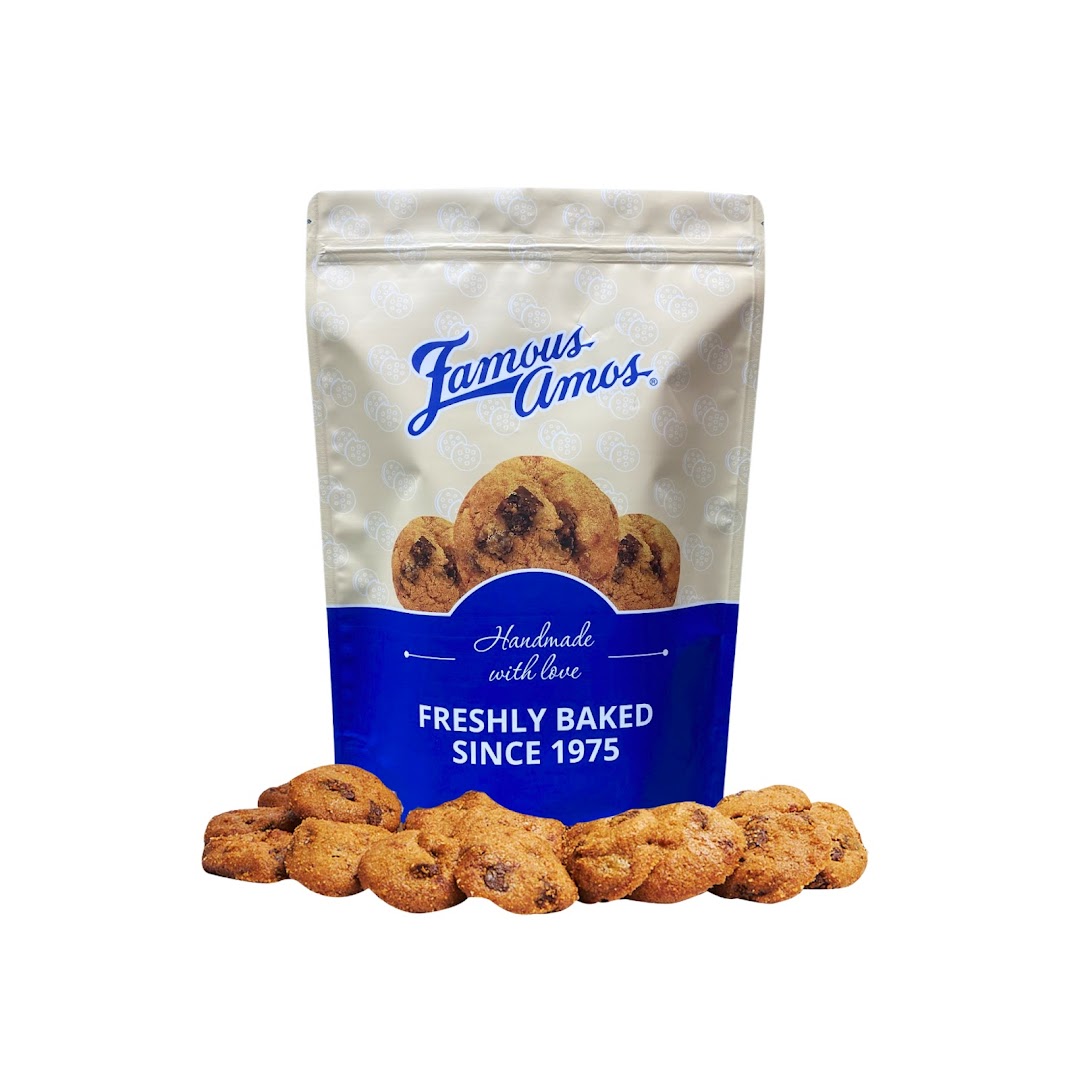 A Famous Amos cookie bag with freshly baked chocolate chip cookies scattered around it.