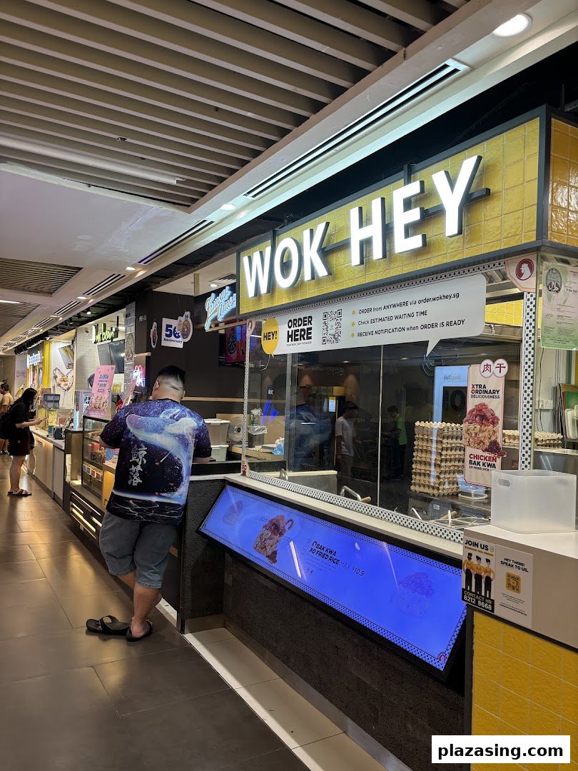 A customer stands at the Wok Hey food stall counter, featuring its bright yellow signage and digital display.