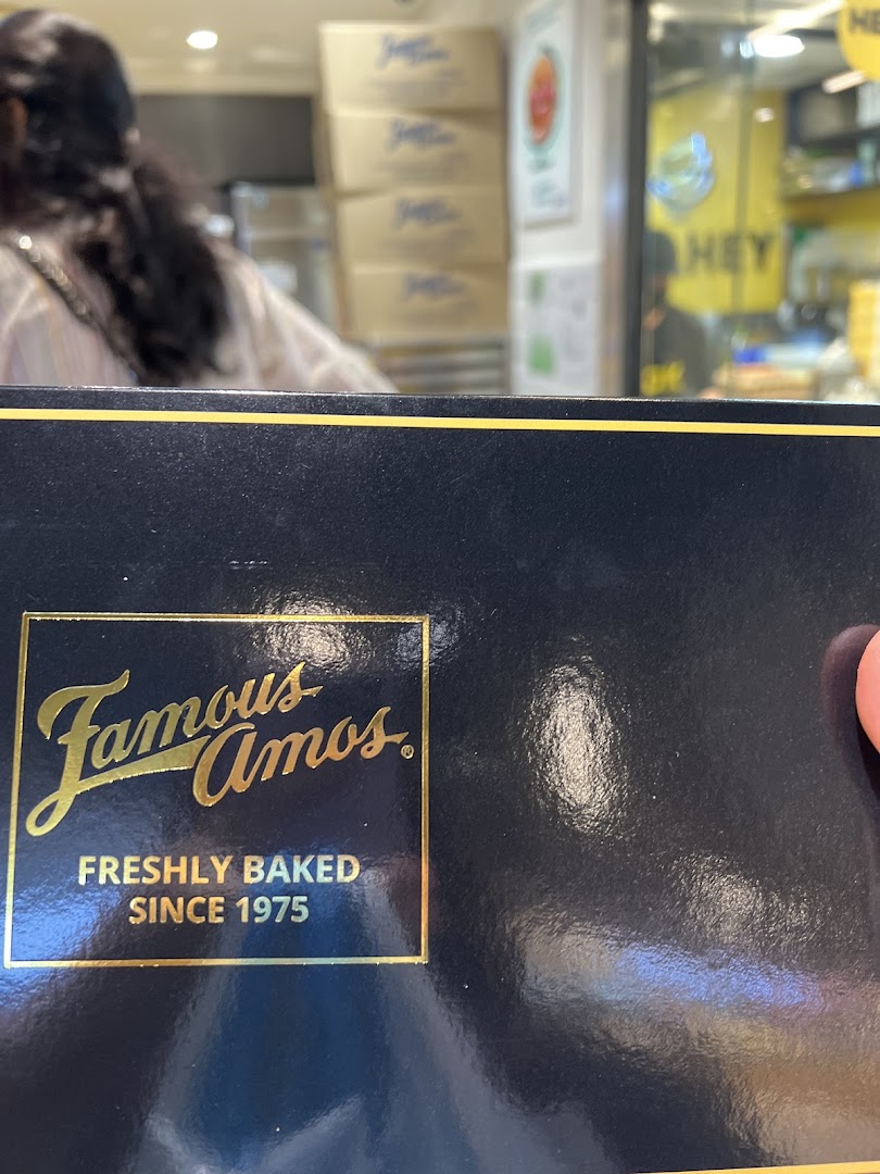 Close-up of a Famous Amos cookie box with the brand logo, showing the shop interior in the background.