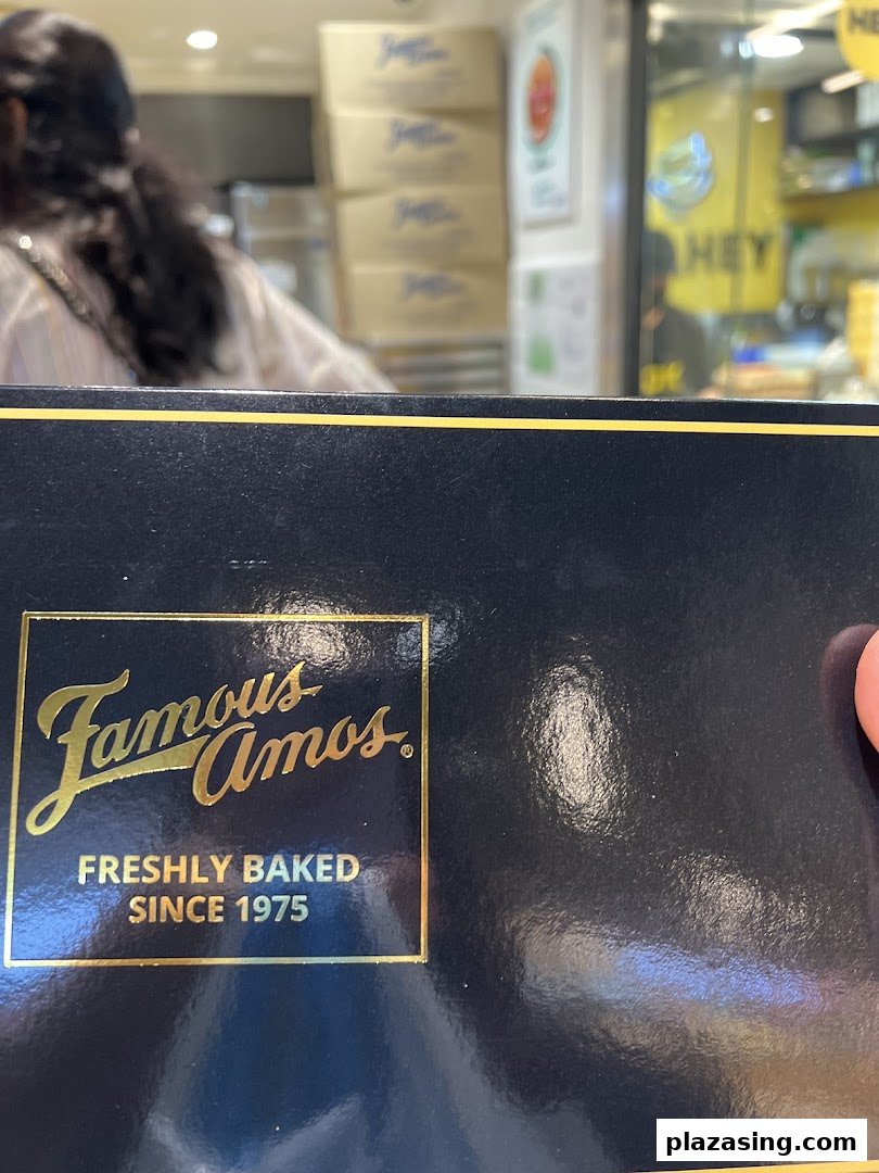 Close-up of a Famous Amos cookie box with the brand logo, showing the shop interior in the background.