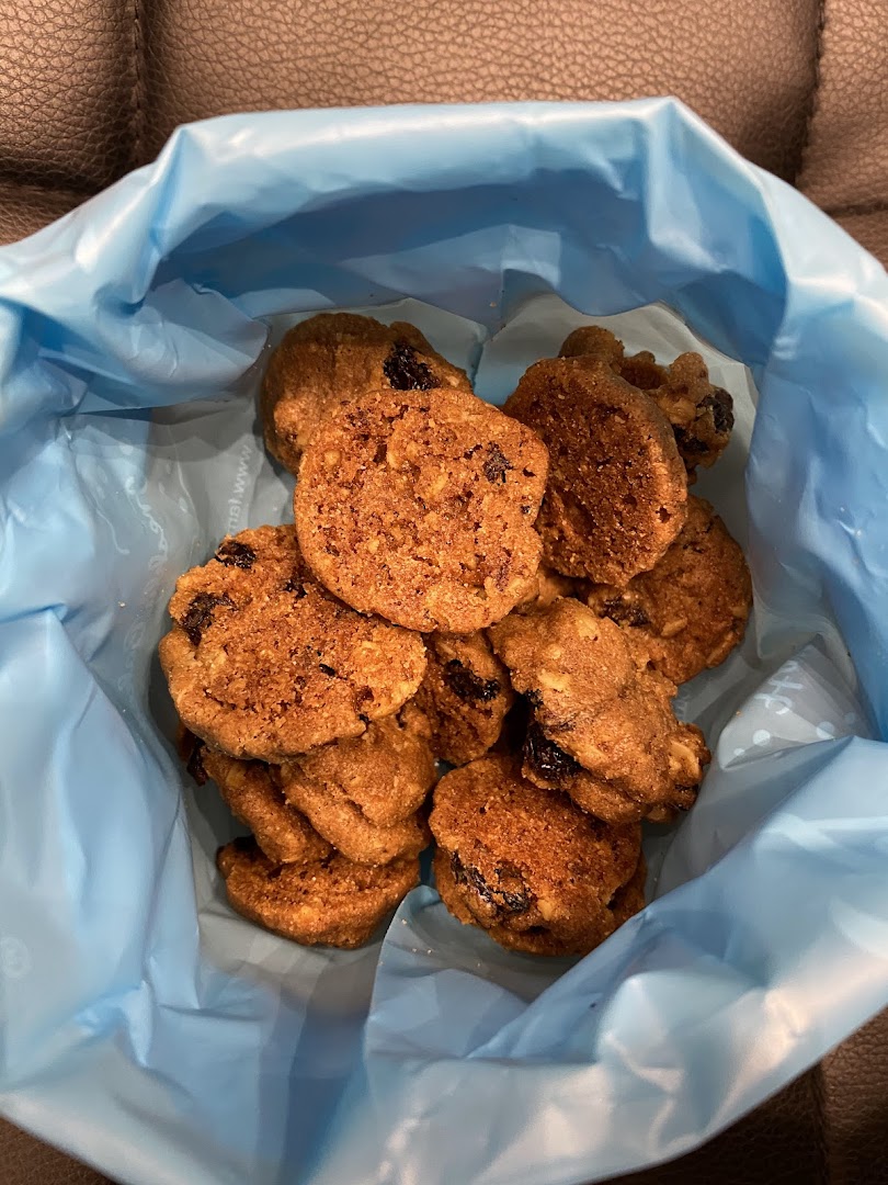 A close-up view of delicious Famous Amos cookies, likely oatmeal raisin, inside a light blue bag.