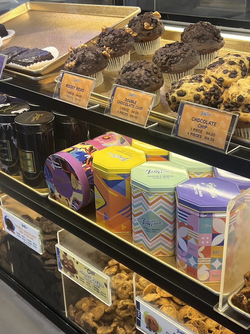 A vibrant display of Famous Amos muffins, cookies, and decorative cookie tins in a retail shop.