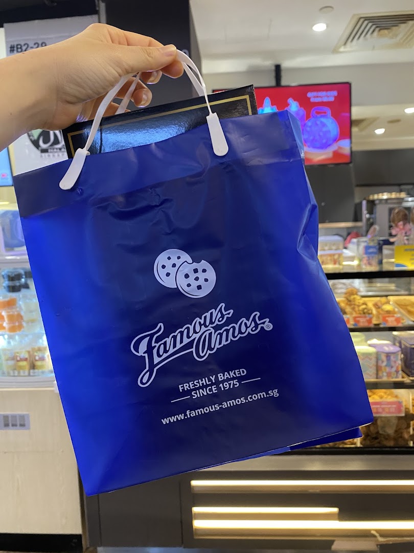 A hand holds a blue Famous Amos shopping bag with cookies logo inside the store.