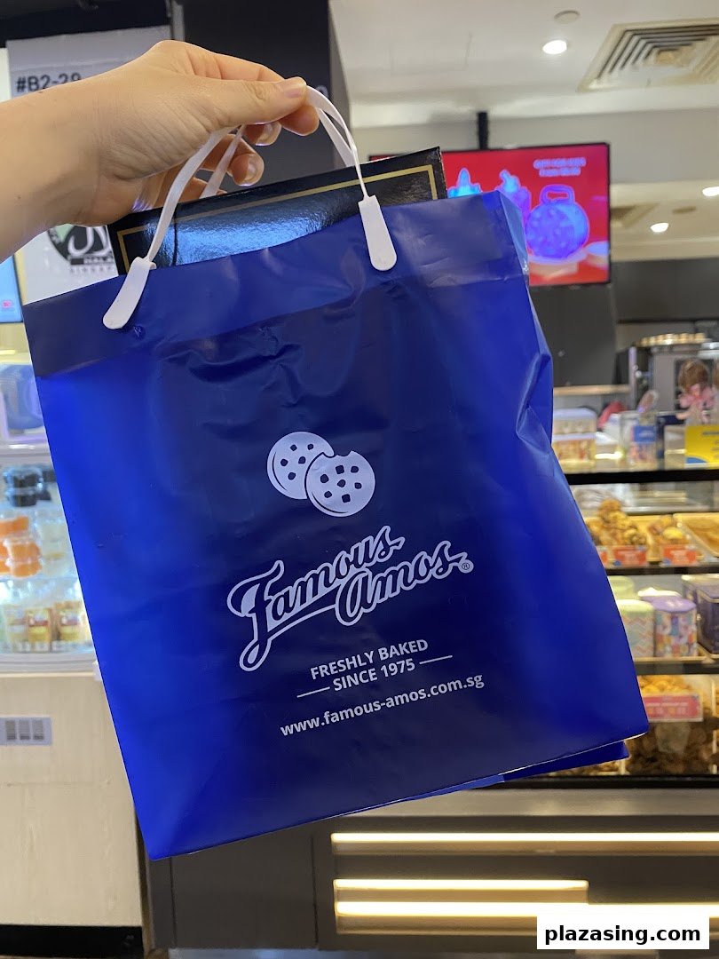 A hand holds a blue Famous Amos shopping bag with cookies logo inside the store.