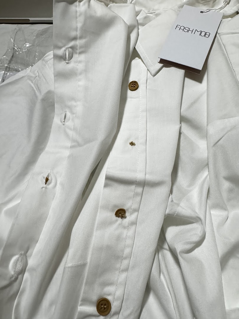 Close-up of a white Fash Mob garment with wooden buttons and brand tag.