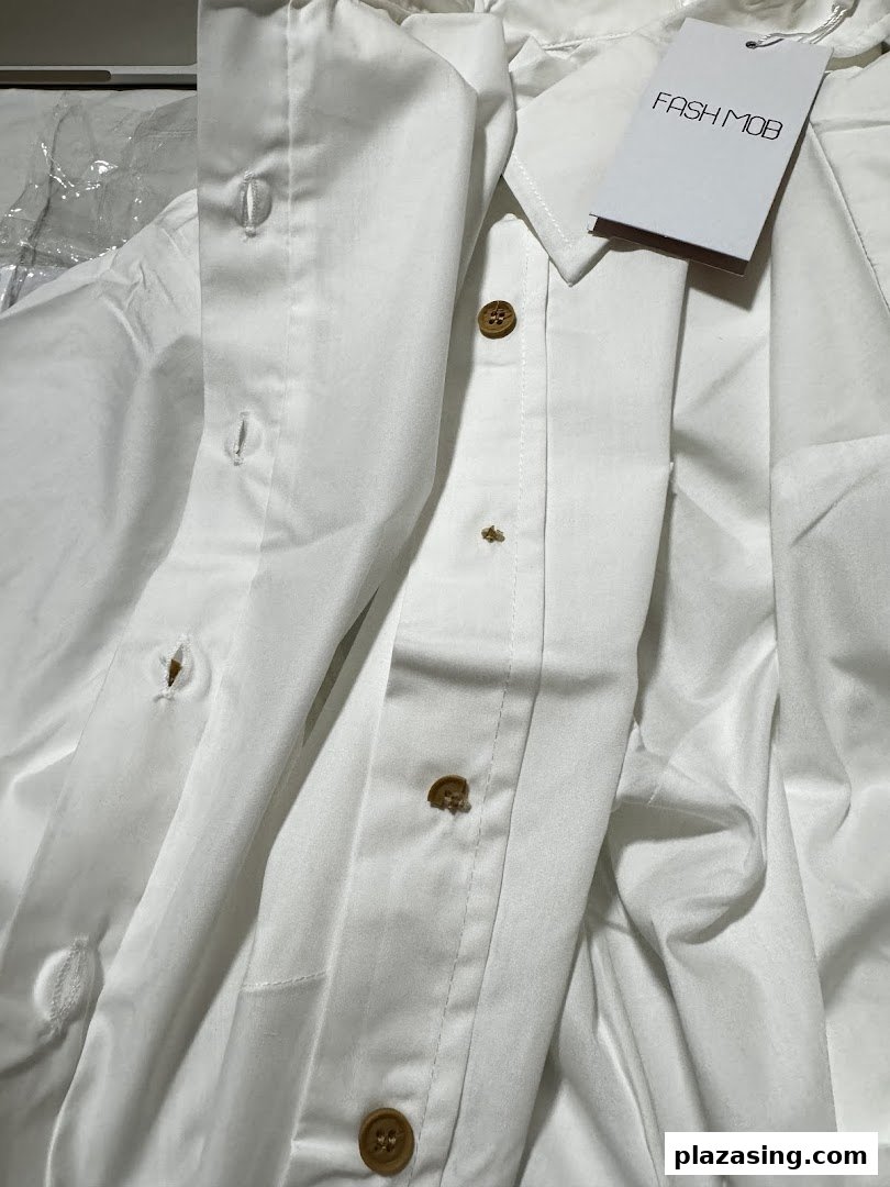 Close-up of a white Fash Mob garment with wooden buttons and brand tag.