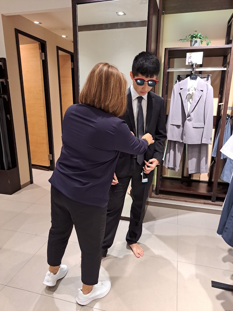 A staff member assists a customer trying on a suit in a G2000 fitting room.