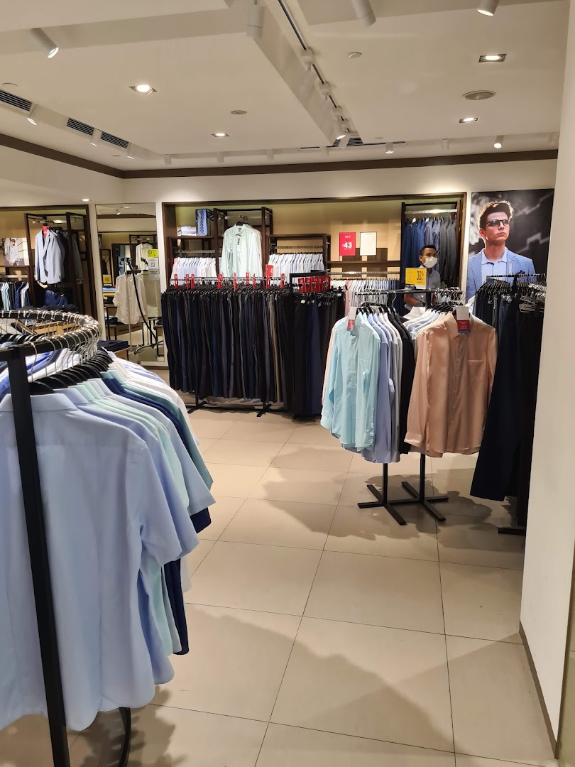 Interior view of G2000, showcasing racks of men's shirts and trousers, with a staff member in the background.