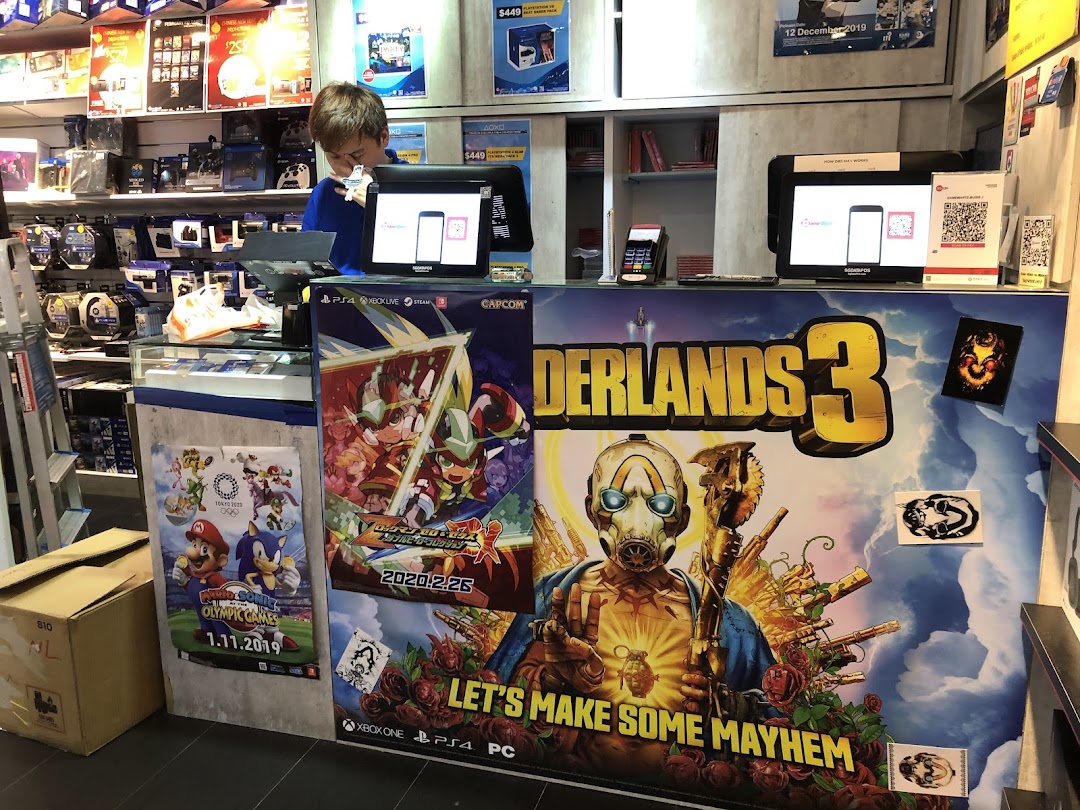 A staff member at the counter of GameMartz Plaza Sing, surrounded by popular game posters and merchandise.