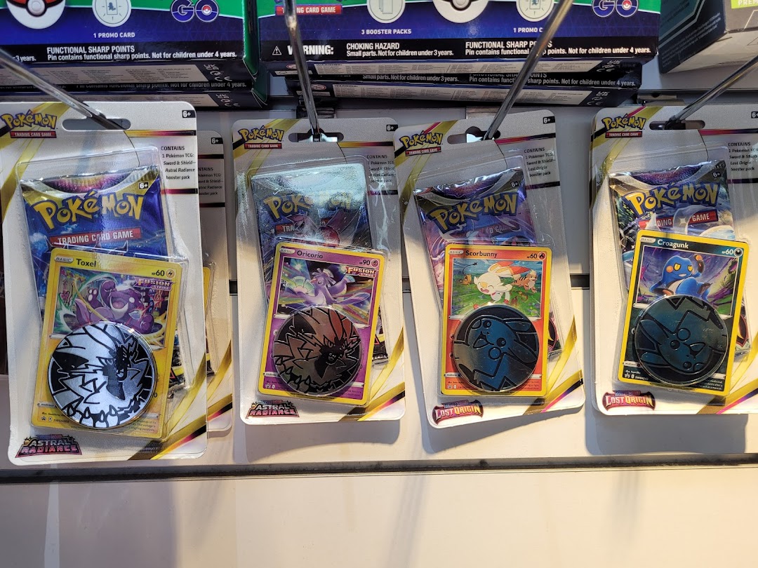Close-up view of various Pokémon Trading Card Game booster packs and collectible cards with coins displayed in a retail store.