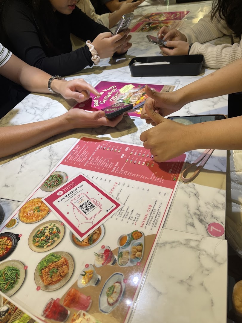 Diners at Go-Ang Pratunam Chicken Rice, with a menu displaying dishes and a QR code.
