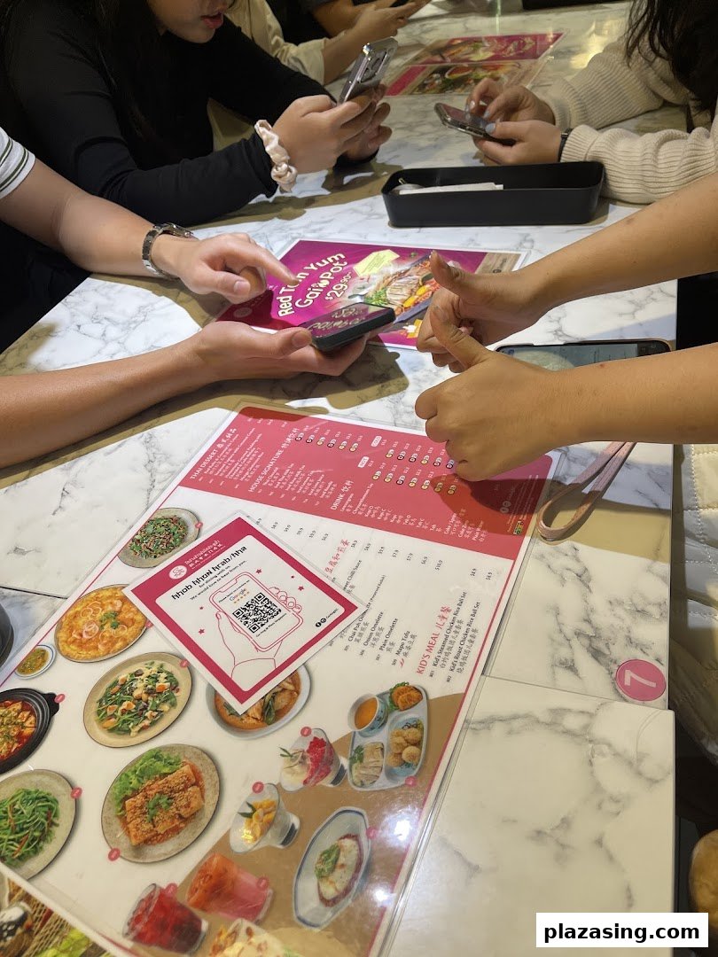 Diners at Go-Ang Pratunam Chicken Rice, with a menu displaying dishes and a QR code.