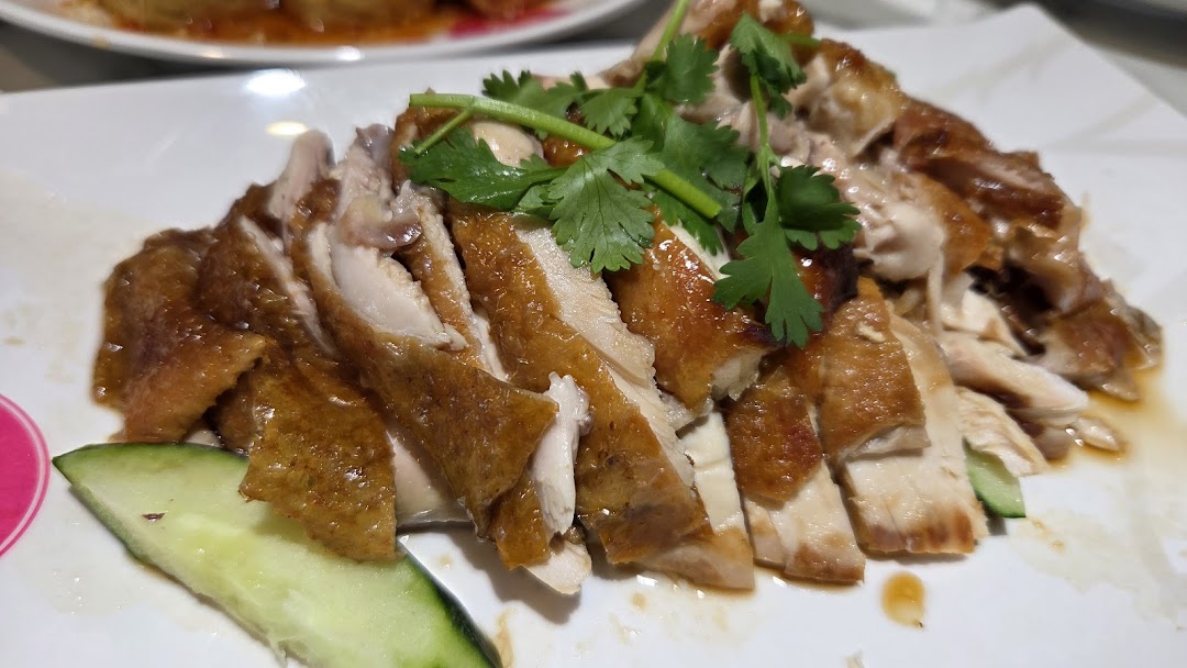 A close-up of succulent sliced roasted chicken with crispy skin, garnished with fresh cilantro and cucumber.