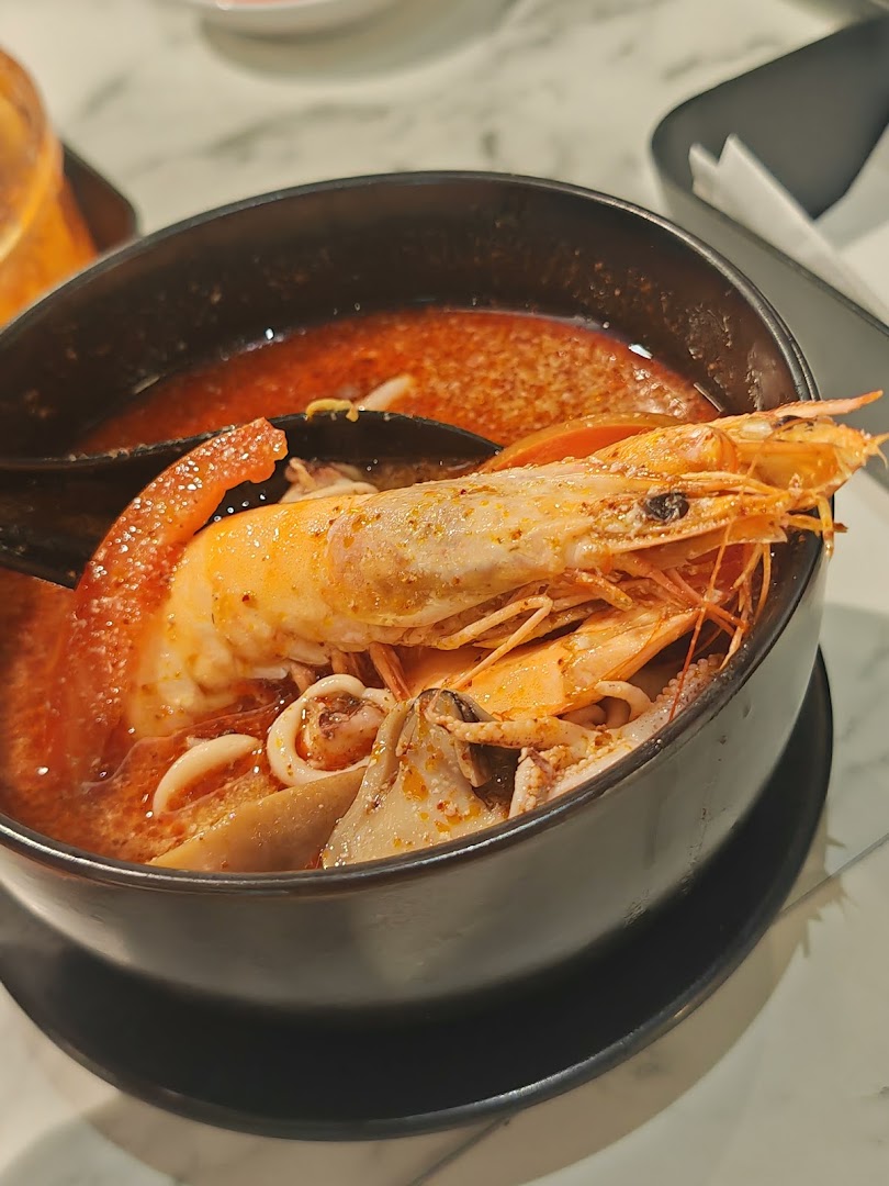 A close-up of a vibrant seafood tom yum soup with large prawns, squid, and mussels in a black bowl.
