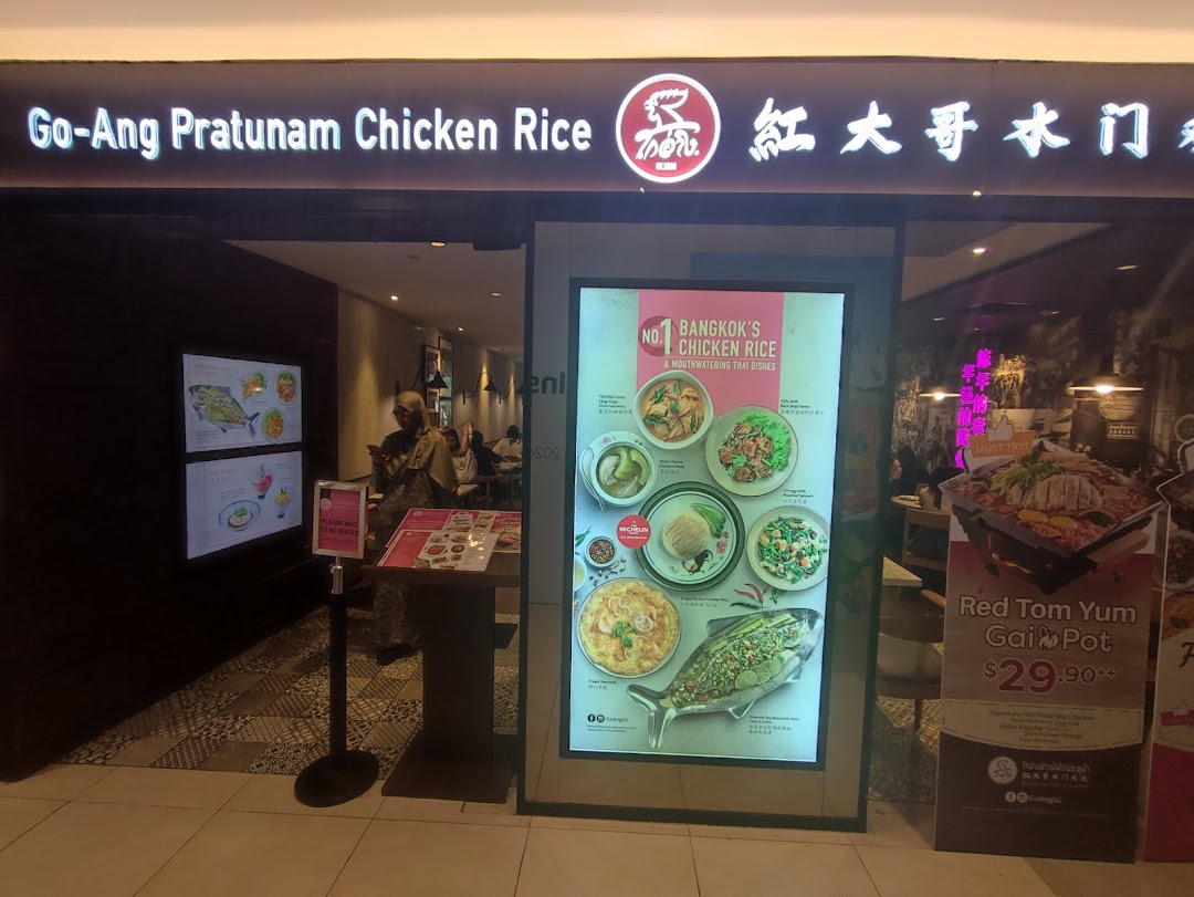 The illuminated storefront of Go-Ang Pratunam Chicken Rice, showcasing its entrance and promotional displays.