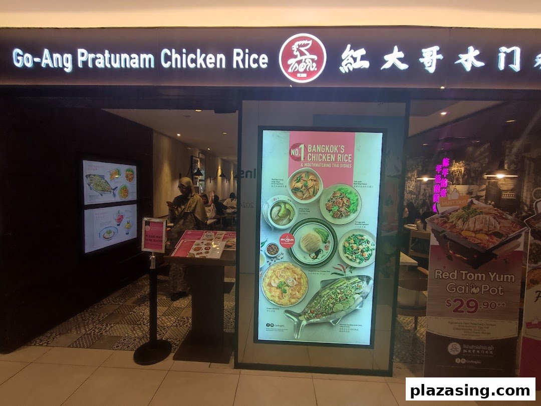 The illuminated storefront of Go-Ang Pratunam Chicken Rice, showcasing its entrance and promotional displays.
