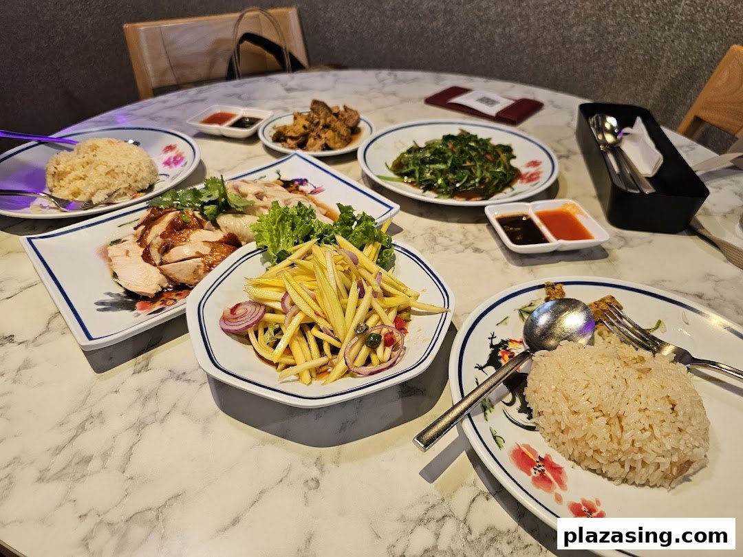 A table laden with various Thai dishes, including chicken rice, mango salad, and stir-fried vegetables.