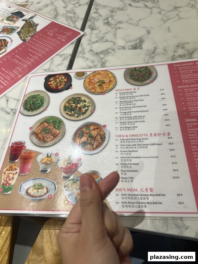 A detailed menu displaying various Thai dishes, including vegetables, tofu, omelettes, and kid's meals, with a hand making a heart gesture.