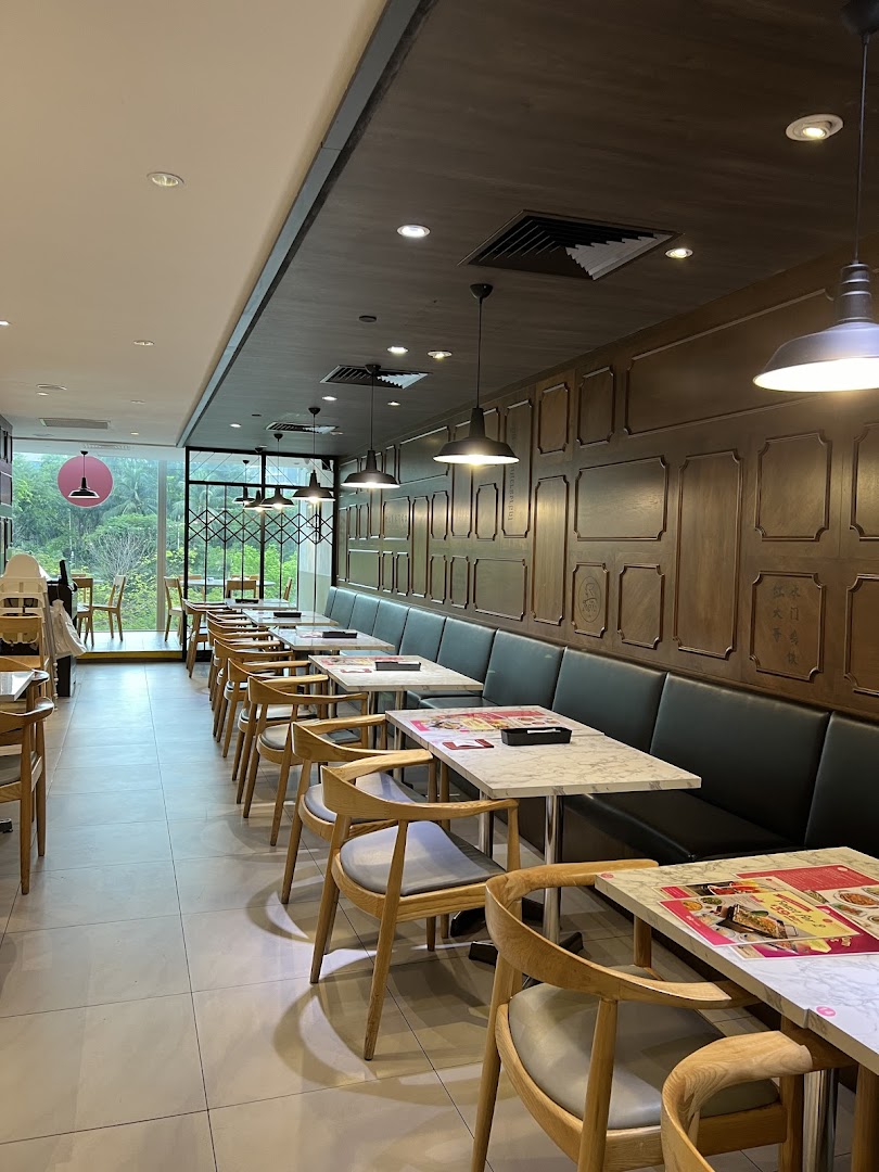 A long, well-lit restaurant interior featuring rows of marble-top tables, wooden chairs, and a window view.