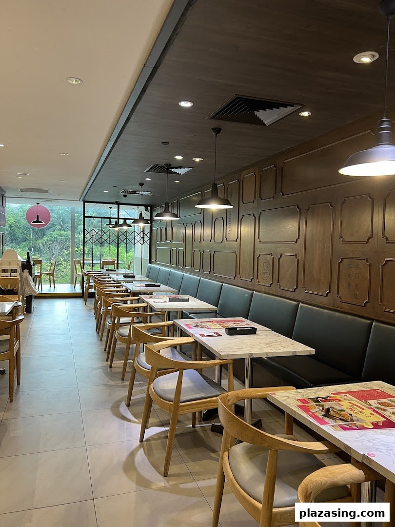 A long, well-lit restaurant interior featuring rows of marble-top tables, wooden chairs, and a window view.