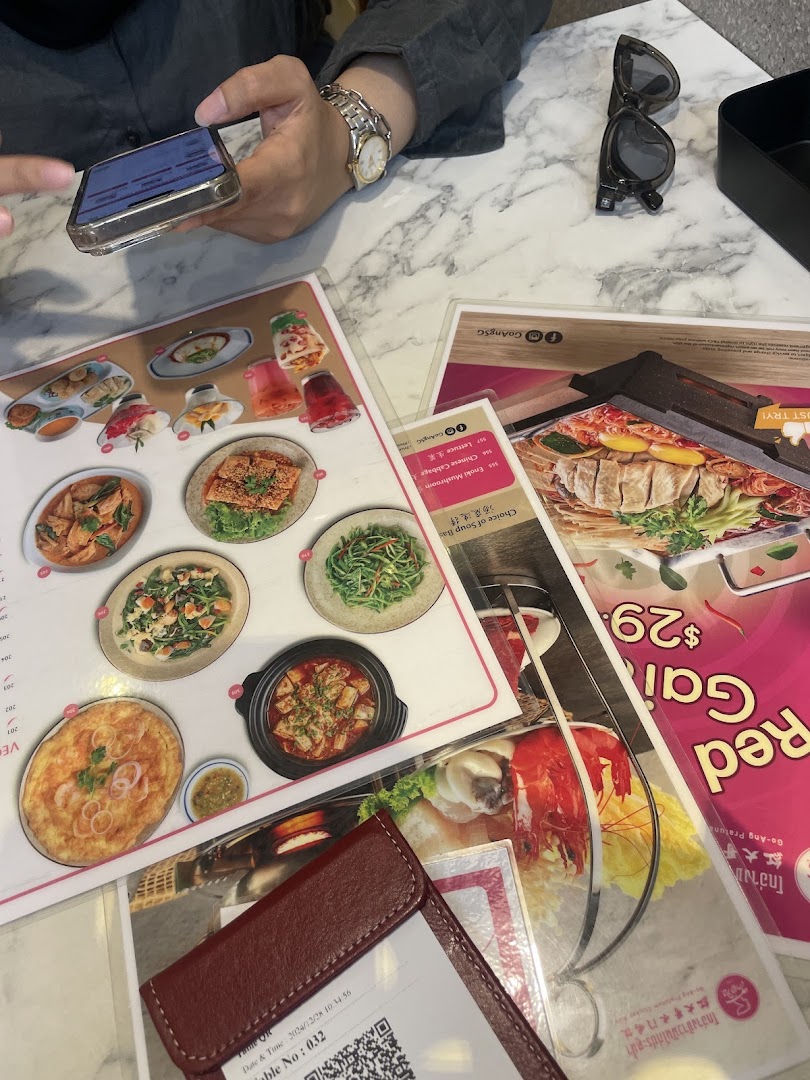 A person's hands are visible at a marble table, browsing multiple menus alongside a phone and sunglasses.
