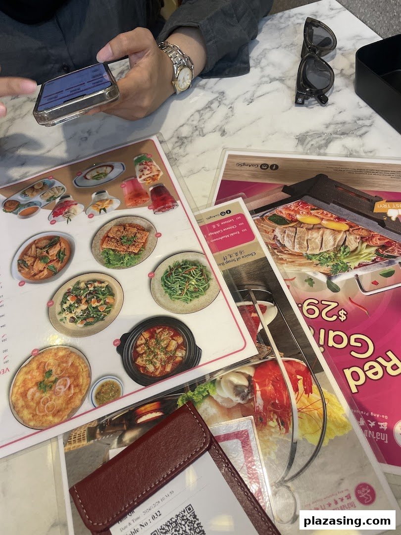 A person's hands are visible at a marble table, browsing multiple menus alongside a phone and sunglasses.