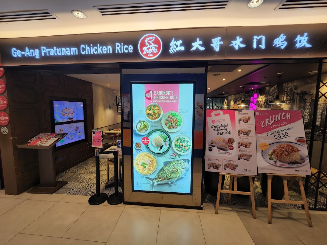 The brightly lit storefront of Go-Ang Pratunam Chicken Rice, showcasing its entrance and promotional displays.
