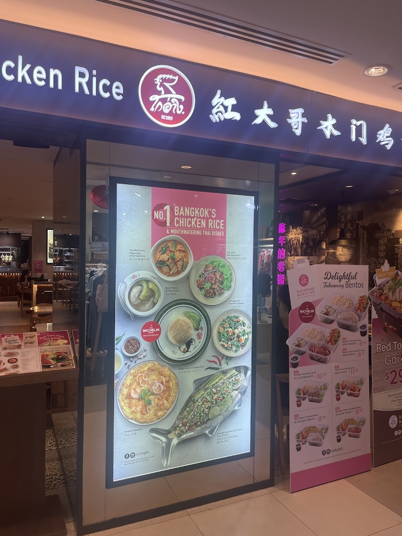 The brightly lit entrance of Go-Ang Pratunam Chicken Rice, showcasing popular Thai dishes and takeaway bentos.
