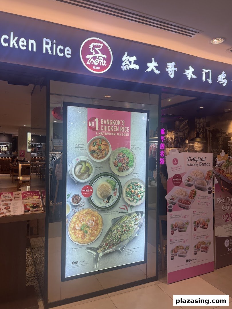 The brightly lit entrance of Go-Ang Pratunam Chicken Rice, showcasing popular Thai dishes and takeaway bentos.