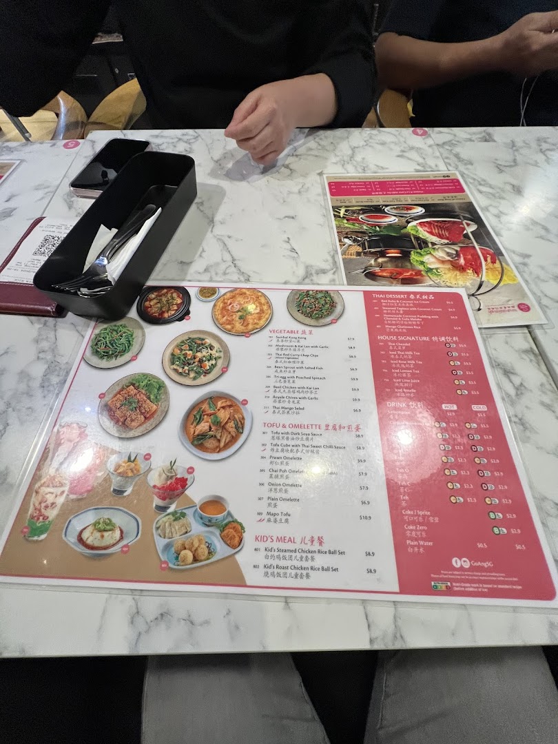 A detailed view of a restaurant menu displaying various Thai dishes, desserts, and drinks on a marble table.