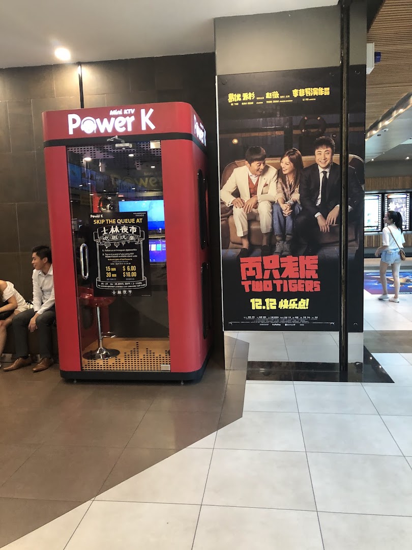 A red Power K mini KTV booth next to a movie poster in a mall setting.