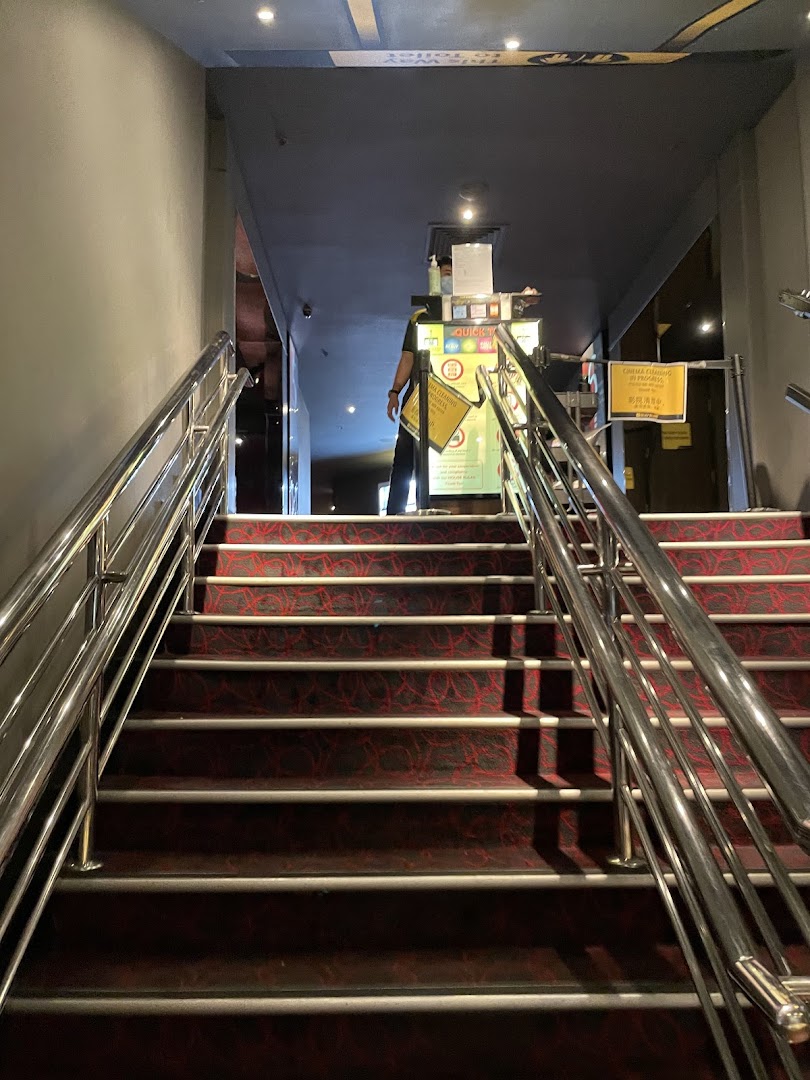 A carpeted staircase with metal railings leading to the entrance of Golden Village Plaza cinema, with a staff member at the counter.