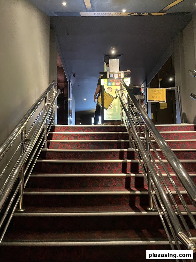 A carpeted staircase with metal railings leading to the entrance of Golden Village Plaza cinema, with a staff member at the counter.