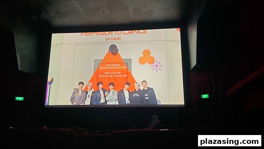 A cinema screen displaying 'Permission to Dance On Stage' content to an audience in a dark theater.