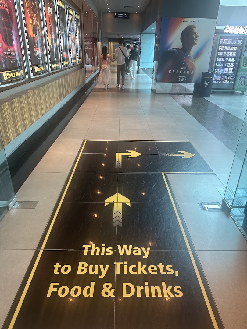 A cinema hallway with movie posters and floor signage directing visitors to ticket and concession stands.
