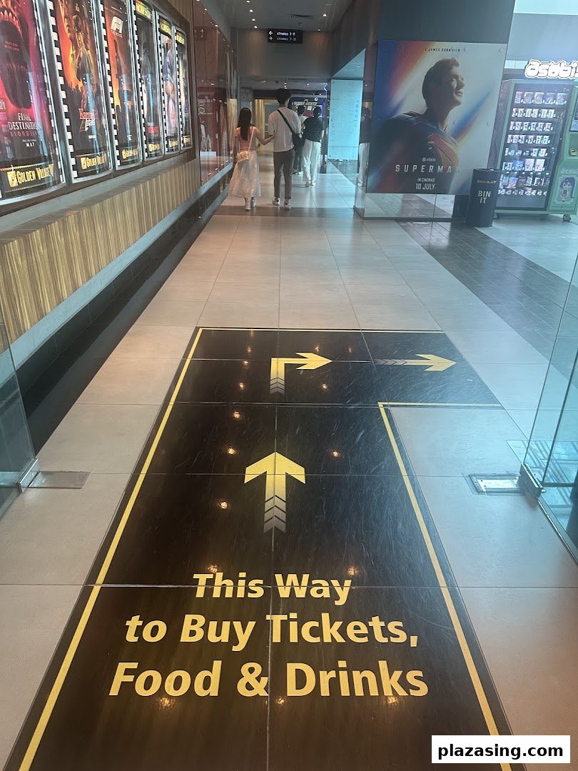 A cinema hallway with movie posters and floor signage directing visitors to ticket and concession stands.