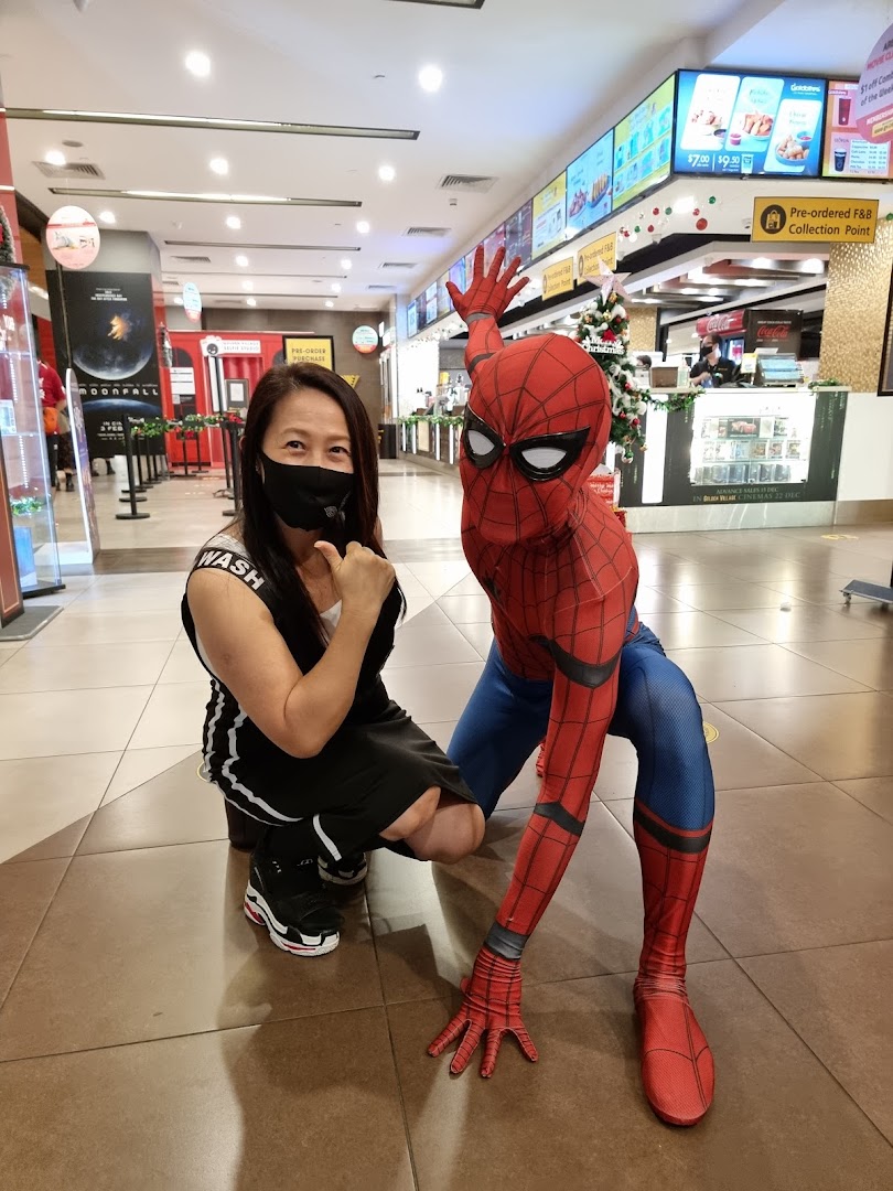 A person poses with a Spiderman character in the lively lobby of Golden Village Plaza cinema.