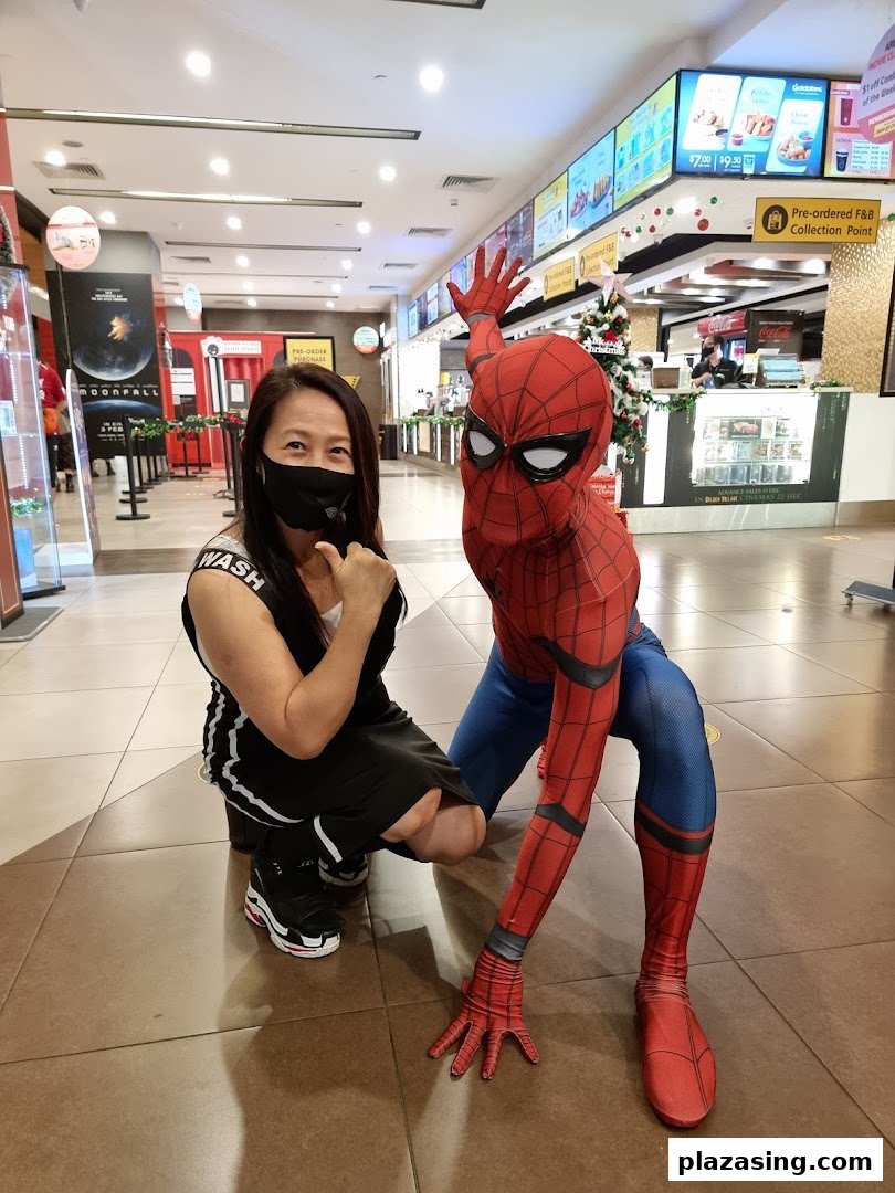 A person poses with a Spiderman character in the lively lobby of Golden Village Plaza cinema.