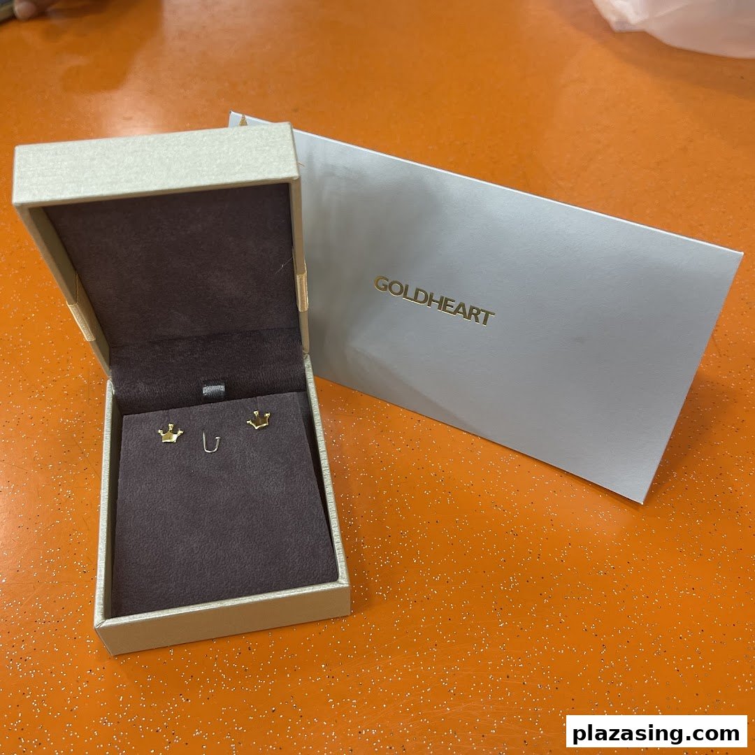 A pair of gold crown earrings displayed in an open Goldheart jewelry box with branded packaging.