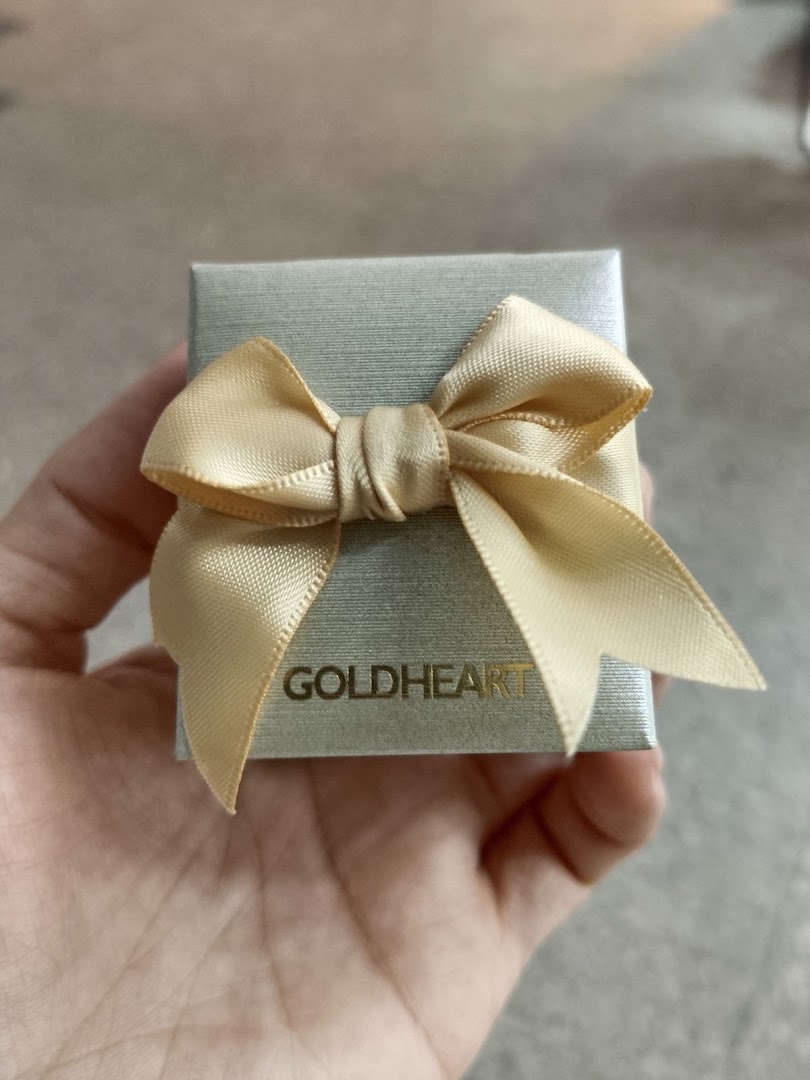 A hand holding a small Goldheart jewelry gift box adorned with a gold ribbon.