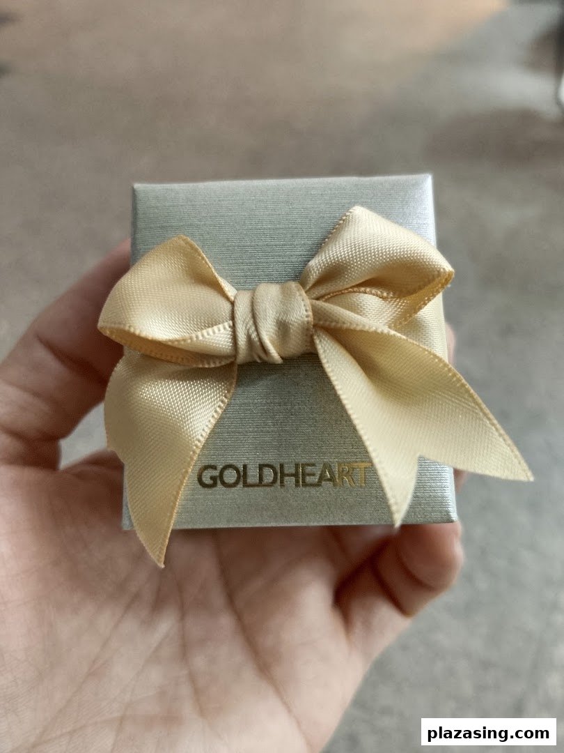 A hand holding a small Goldheart jewelry gift box adorned with a gold ribbon.