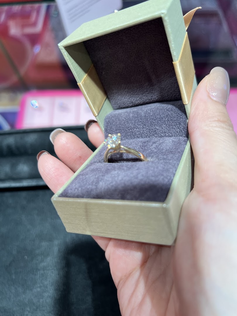 A hand holds an open jewelry box revealing a sparkling diamond ring.