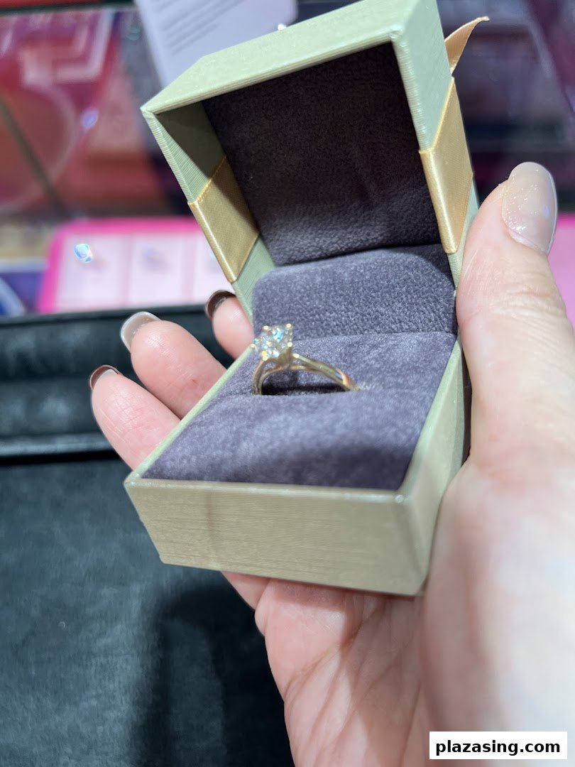 A hand holds an open jewelry box revealing a sparkling diamond ring.