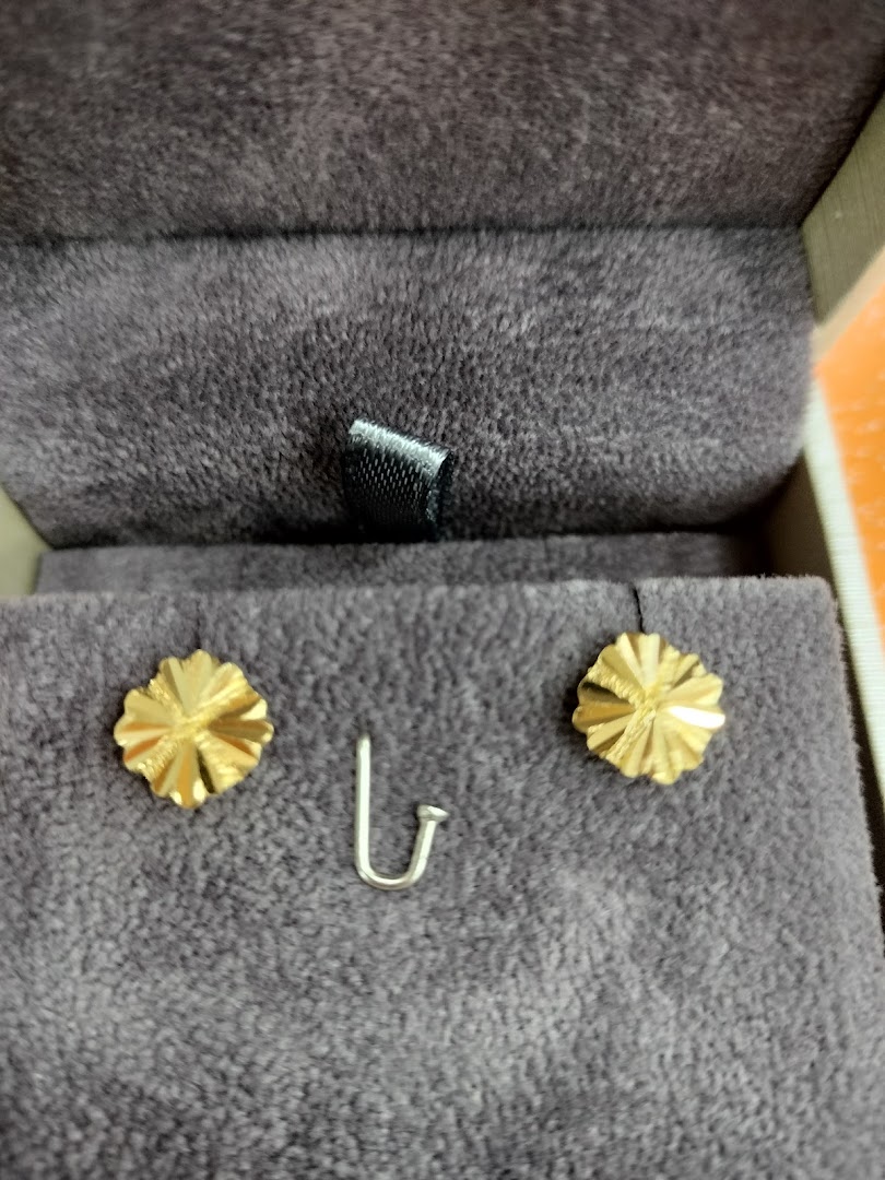 Two gold flower-shaped earrings and a silver hook displayed in a velvet jewelry box.