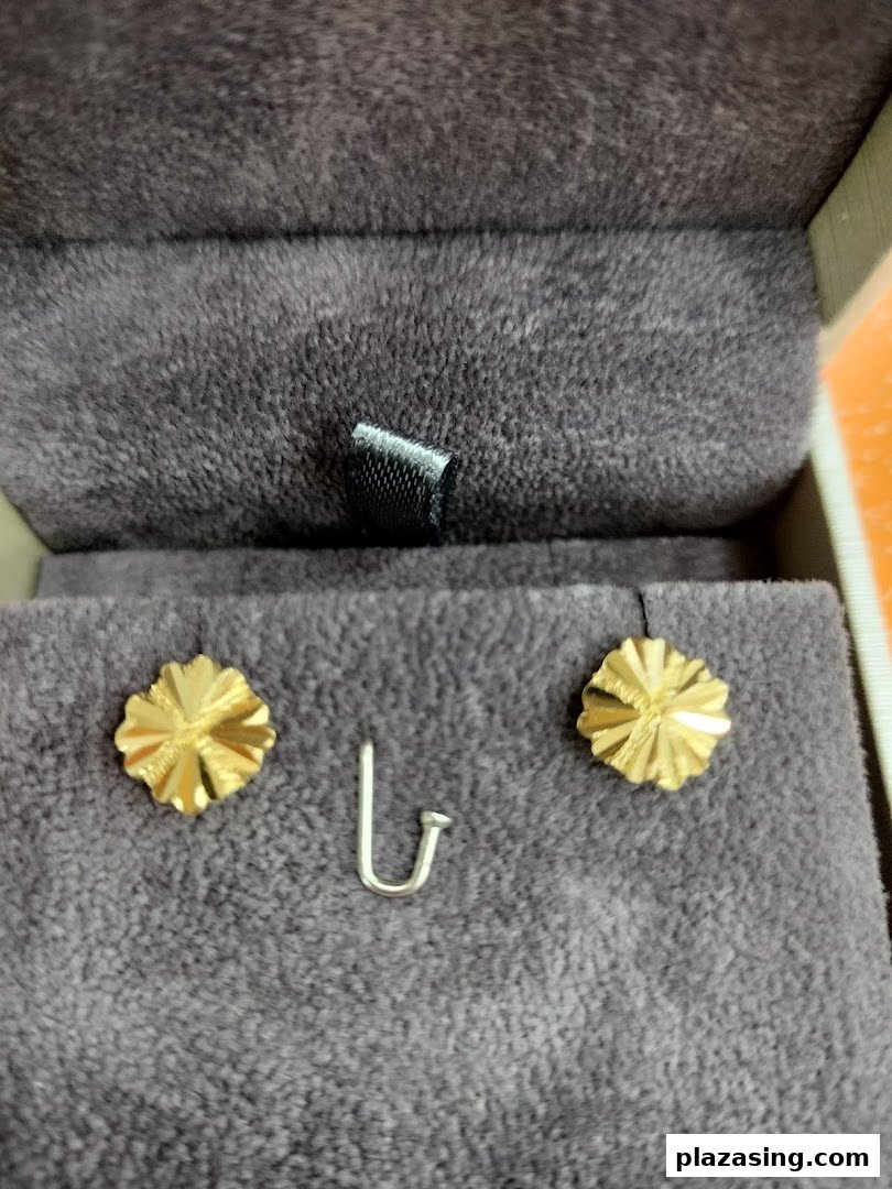 Two gold flower-shaped earrings and a silver hook displayed in a velvet jewelry box.