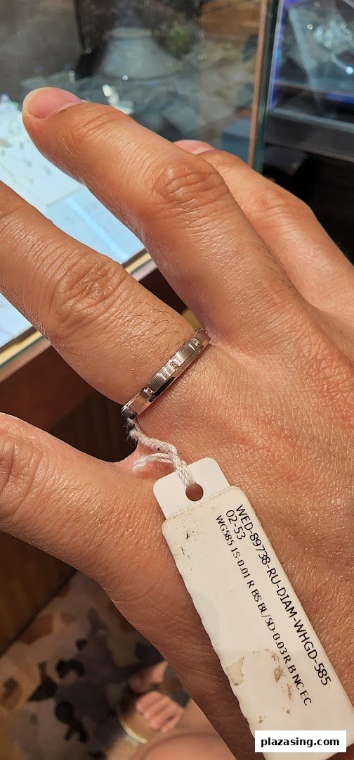 A hand wearing a diamond ring with a product tag attached, likely inside a jewelry store.