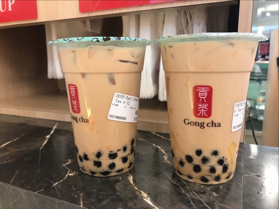 Two refreshing Gong Cha bubble tea drinks with pearls on a dark counter.
