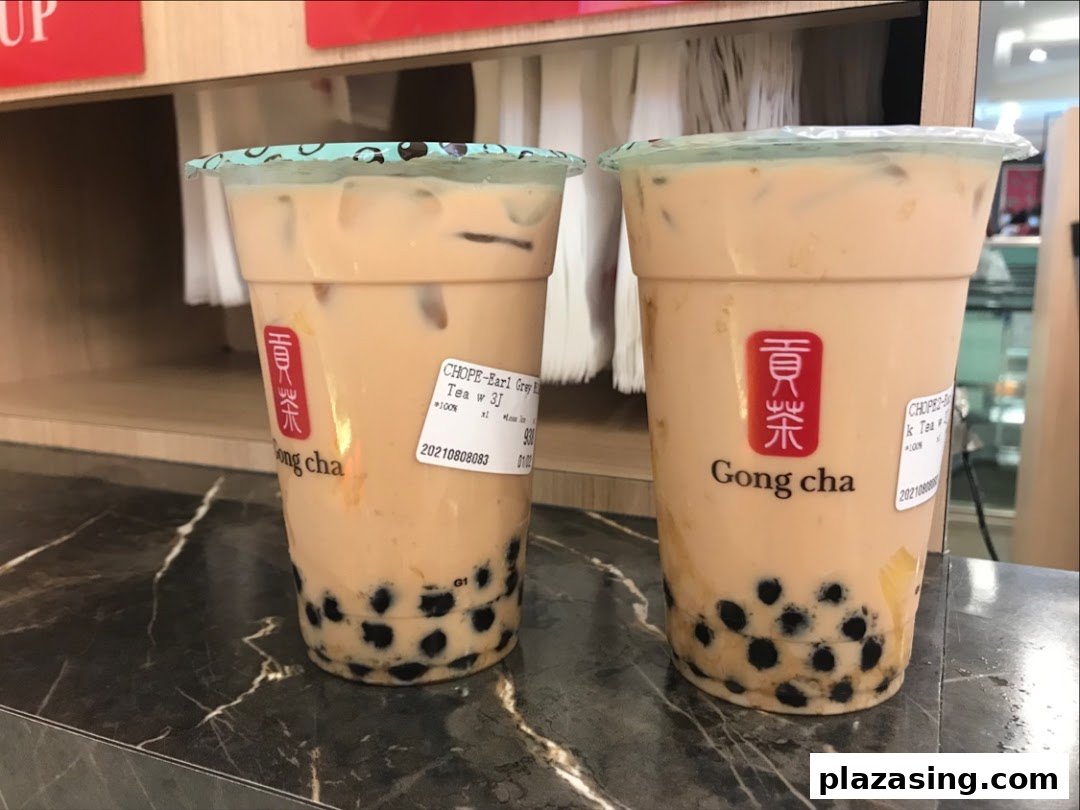 Two refreshing Gong Cha bubble tea drinks with pearls on a dark counter.
